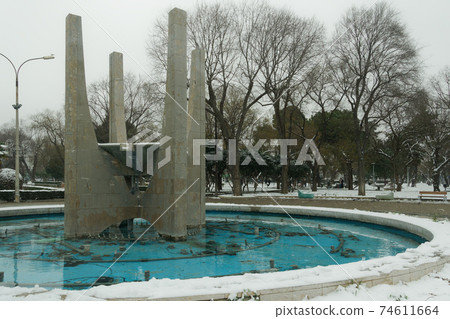 Stopped water fountain not working during snowfall at a city center. 74611664