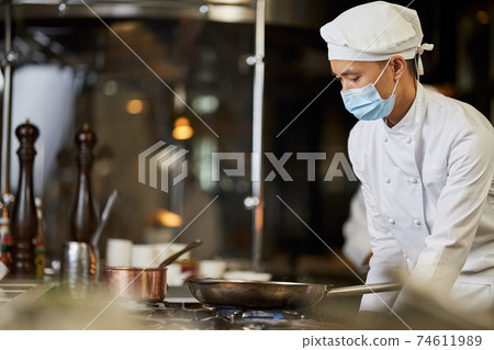 Focused Asian chef observing pans on the stove Focused Asian chef observing pans on the stove 74611989