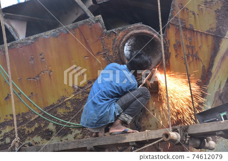 Dhaka, Bangladesh, Shodrugat, a mechanic repairing an old passenger ship, processing metal on the hull 74612079