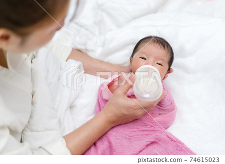 mother feeding milk bottle to her newborn baby on bed 74615023