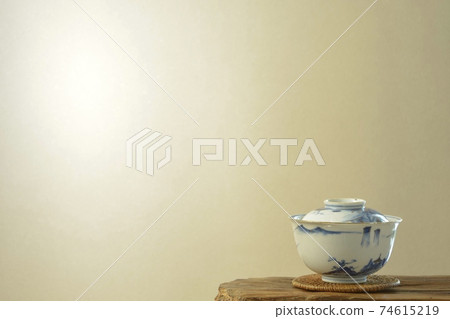 Antique Imari ware ceramics. Teacup with lid on display shelf (bright wall, soft focus) Antique Imari ware ceramics. Teacup with lid on display shelf (bright wall, soft focus) 74615219