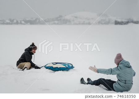 Man pulling snow tube with girlfriend. Young happy couple walking in winter day 74618350