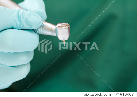 Dentist's hand in glove with dental handpiece. 74619408