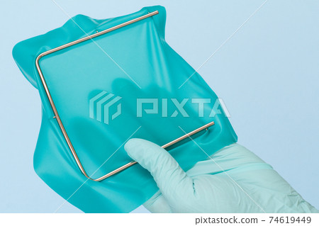 Dentist's hand in glove with dental cofferdam scarf and metal frame. 74619449