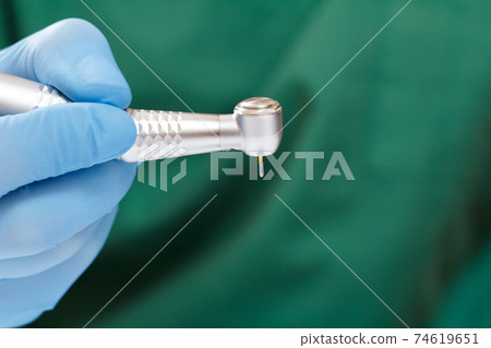 Dentist's hand in glove with dental handpiece. 74619651