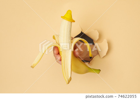 Female hand hold banana with condom through the paper 74622055