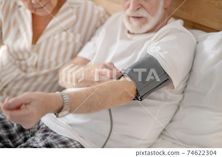 Grey-haired elderly man checking his blood pressure and looking concentrated 74622304