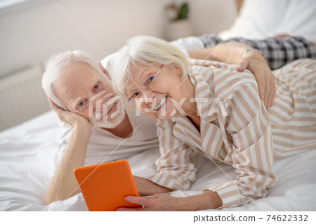Grey-haired woman showing something on a tablet to her husband Grey-haired woman showing something on a tablet to her husband 74622332