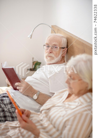Aged married couple lying in bed and reading and feeling good Aged married couple lying in bed and reading and feeling good 74622338