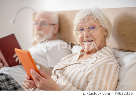 Aged married couple lying in bed and reading and feeling good Aged married couple lying in bed and reading and feeling good 74622339