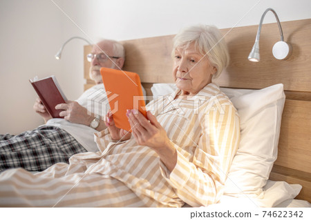 Aged married couple lying in bed and reading Aged married couple lying in bed and reading 74622342