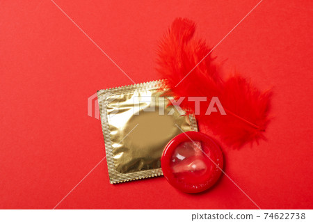 Condoms and red feather on red background 74622738