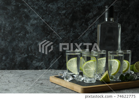 Board with bottle and shots of vodka with lime on gray table Board with bottle and shots of vodka with lime on gray table 74622775