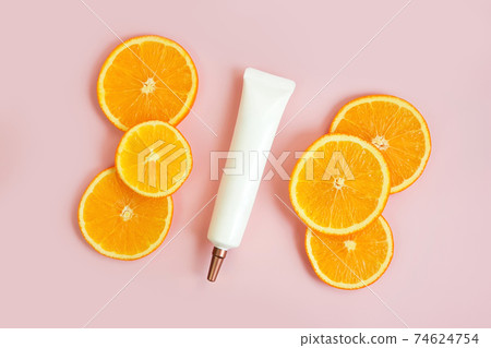Top view of face and eye cream squeeze cosmetic tube with long nozzle and bronze screw cap and orange slices on powdery pink background. Stylish branding mockup, flat lay. Top view of face and eye cream squeeze cosmetic tube with long nozzle and bronze screw cap and orange slices on powdery pink background. Stylish branding mockup, flat lay. 74624754