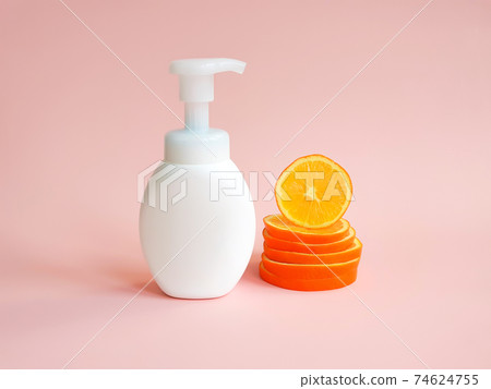 White unbranded bottle with pump and orange slices  on light pink background. Blank container for lotion, cream, sunscreen, shampoo or hair conditioner. Mockup style, cosmetic products advertising 74624755