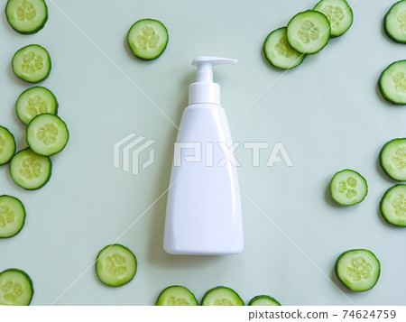 White pump cream bottle and fresh cucumber slices on green background. Liquid soap or cleansing cream bottle. Cosmetic packaging mockup with copy space, template, front view White pump cream bottle and fresh cucumber slices on green background. Liquid soap or cleansing cream bottle. Cosmetic packaging mockup with copy space, template, front view 74624759