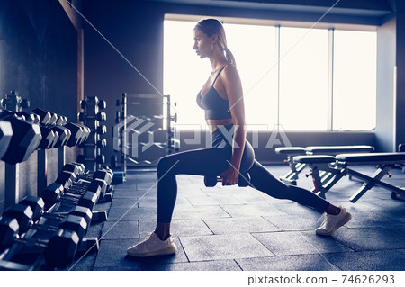 Woman doing lunges exercise with dumbbells in gym 74626293