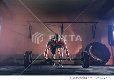 Muscular fitness man doing push a barbell over his head in his g Muscular fitness man doing push a barbell over his head in his g 74627689
