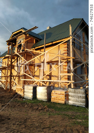 Insulation of the house with facade bricks, construction of a new house and scaffolding near the walls. 74627938