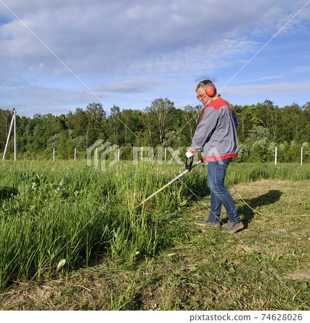 Man mows the grass with a trimmer, tall grass in a meadow, handmade in the garden. 74628026