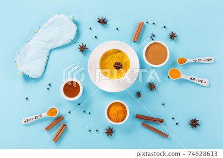Turmeric golden milk latte with spices, cinnamon, honey and Sleep mask on blue background. Top view, copy space. Turmeric golden milk latte with spices, cinnamon, honey and Sleep mask on blue background. Top view, copy space. 74628613