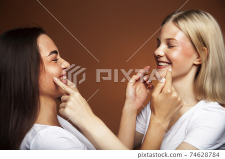 two pretty diverse girls happy posing together: blond and brunette, caucasian and asian on brown background, lifestyle people concept two pretty diverse girls happy posing together: blond and brunette, caucasian and asian on brown background, lifestyle people concept 74628784
