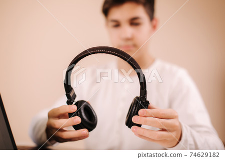 Close up steamer hold on-ear wireless headphones in hand and prepare for playing game. Teenage use laptop Close up steamer hold on-ear wireless headphones in hand and prepare for playing game. Teenage use laptop 74629182