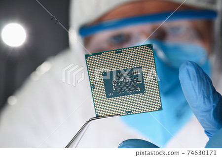 Researcher holds small microcircuit with tongs closeup Researcher holds small microcircuit with tongs closeup 74630171