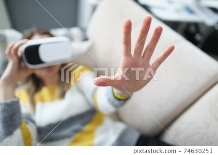 Woman in virtual reality glasses lies on couch and holds her hand up Woman in virtual reality glasses lies on couch and holds her hand up 74630251