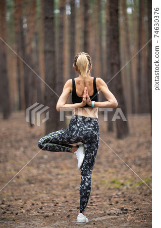 Beautiful woman standing and doing yoga in forest. Exercise and 74630376