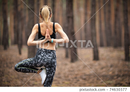 Beautiful woman standing and doing yoga in forest. Exercise and 74630377