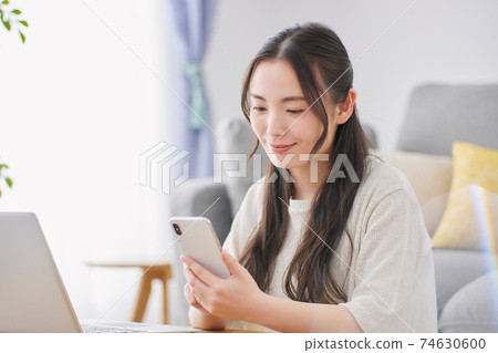 A young woman operating a smartphone in the living room A young woman operating a smartphone in the living room 74630600