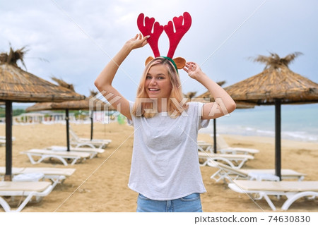 Beautiful young woman walking on the beach in Christmas deer ears Beautiful young woman walking on the beach in Christmas deer ears 74630830