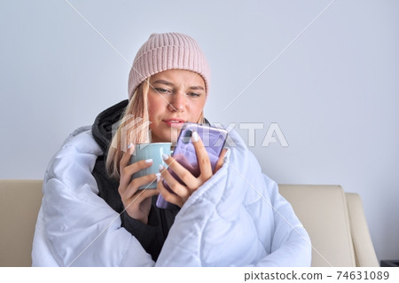 Cold autumn winter season, teenage girl sitting under blanket using smartphone Cold autumn winter season, teenage girl sitting under blanket using smartphone 74631089