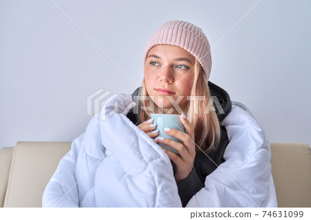 Cold autumn winter season, teenage girl sitting on sofa under warm blanket 74631099