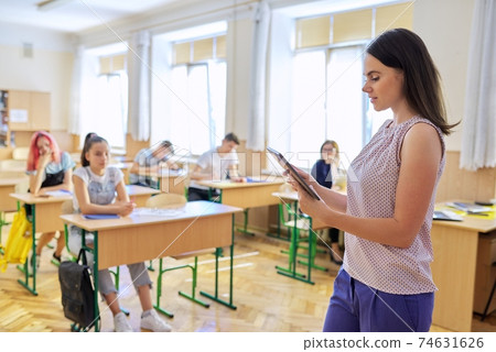 Portrait of young smiling confident female teacher with digital tablet in classroom 74631626