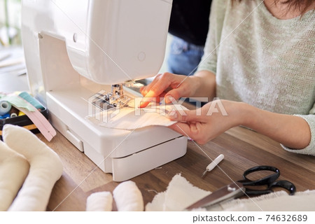 Adult woman sews on a sewing machine sitting at home at table Adult woman sews on a sewing machine sitting at home at table 74632689