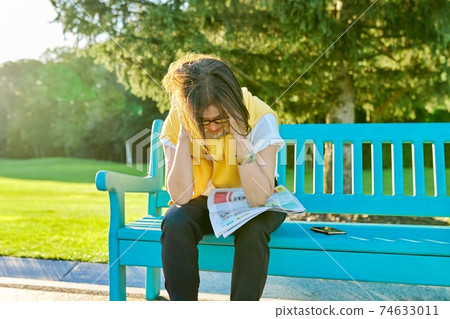 Upset mature woman with newspaper on bench in park, bad news 74633011