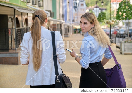 Back shot of two young business women walking and talking in the city Back shot of two young business women walking and talking in the city 74633365