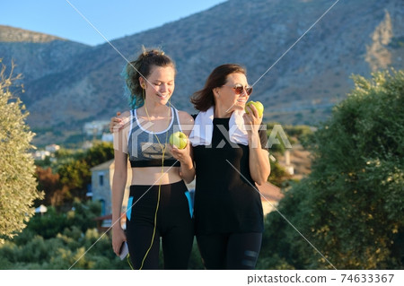 Mother and teenage daughter eating apples after jogging on sunset mountain road Mother and teenage daughter eating apples after jogging on sunset mountain road 74633367