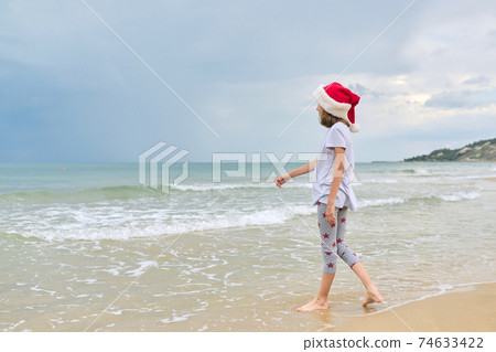 Background sea ocean beach, child girl in Santa hat having fun, back view Background sea ocean beach, child girl in Santa hat having fun, back view 74633422