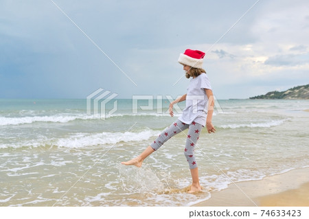 Background sea ocean beach, child girl in Santa hat having fun, back view Background sea ocean beach, child girl in Santa hat having fun, back view 74633423
