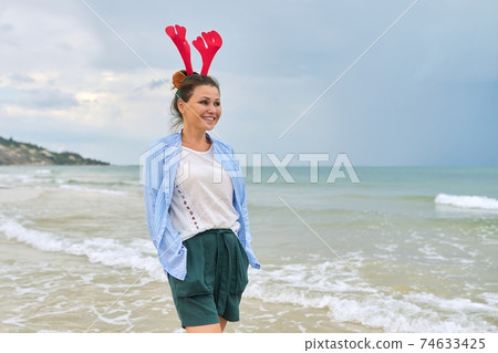 Portrait of happy mature woman in holiday ears on beach 74633425