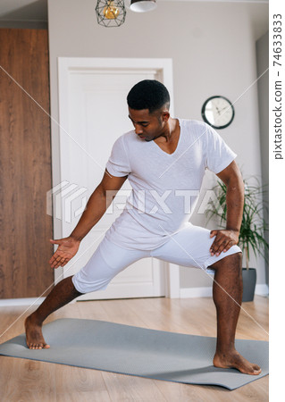 Focused fit African-American man making sport fitness exercise standing on yoga mat. 74633833