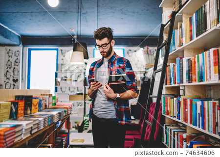 Positive young man using free 4G internet on cellular in library Positive young man using free 4G internet on cellular in library 74634606