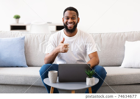 Black Man At Laptop Gesturing Thumbs-Up To Camera At Home Black Man At Laptop Gesturing Thumbs-Up To Camera At Home 74634677