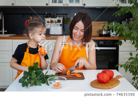 Little girl and beautiful mom are cooking vegetables at home kitchen 74635398