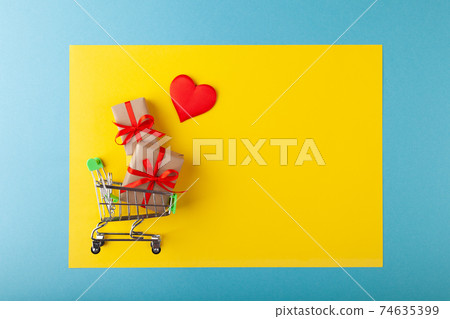 Red heart, gift box with red ribbon inside mini grocery cart on colored background Red heart, gift box with red ribbon inside mini grocery cart on colored background 74635399