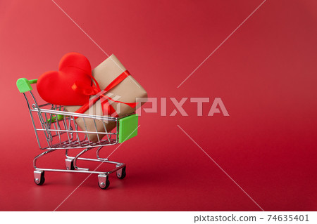 Red heart, gift box with red ribbon inside mini grocery cart on colored background Red heart, gift box with red ribbon inside mini grocery cart on colored background 74635401