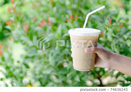 Close up hand holding glass of ice coffee with green leaves nature background, selective focus Close up hand holding glass of ice coffee with green leaves nature background, selective focus 74636245